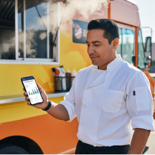 A confident food truck operator reviewing a 'Profit by Location' report on a smartphone, with their successful food truck in the background.